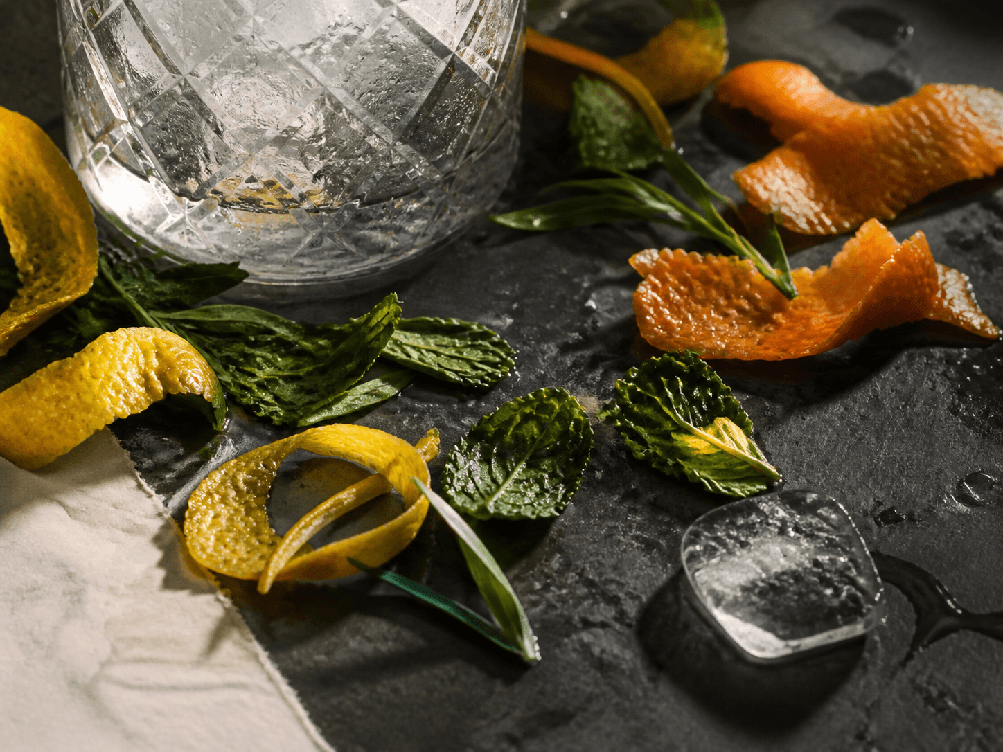 Citrus peel, herbs, ice, and chilled glassware on a bar