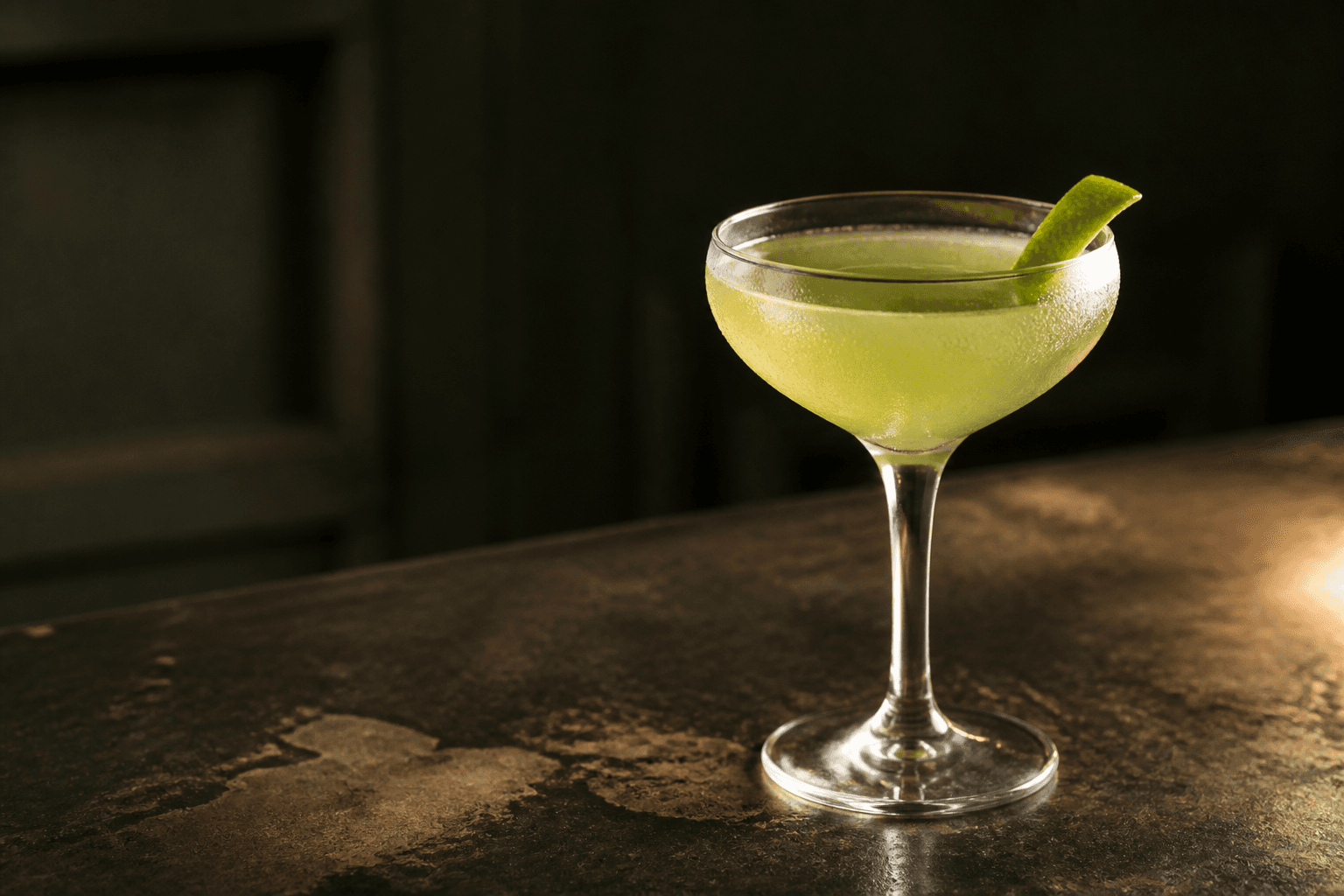 A pale green cocktail with a lime twist